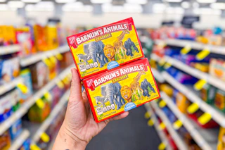 person holding 2 boxes of barnums animal crackers in an aisle