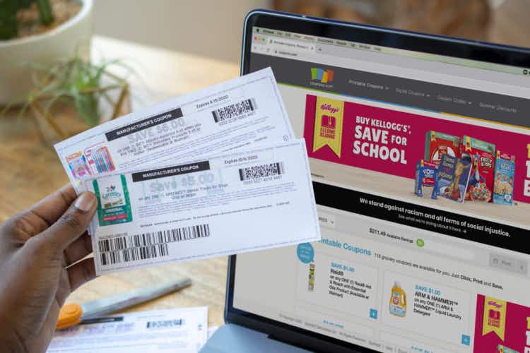 A person holding coupons next to the coupons.com website open on a computer screen.
