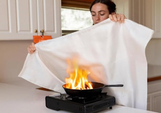 a person holding a fire-proof blanket over a skillet on fire
