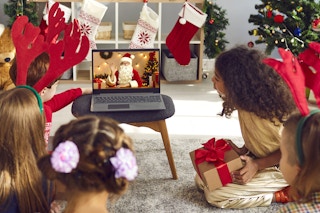 children in living room talking to santa claus on video call laptop