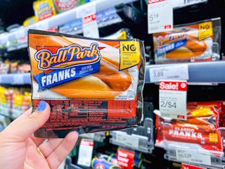 hand holding Ball Park franks next to sales tag