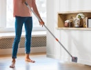 a person cleaning the baseboards with a mop