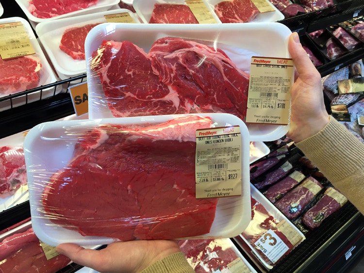 A shopper comparing two packages of meat in a store.