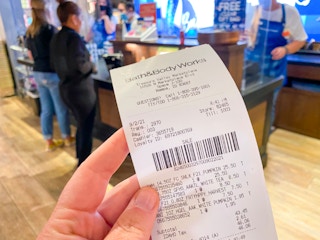 Hand holding Bath & Body Works receipt in store with checkout counter in the background