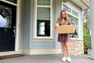 A person standikng on a porch while holding a box.