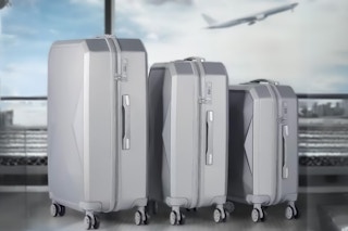 Lifestyle image of a hard-sided 3-piece luggage set displayed in airport with plane taking off in the background