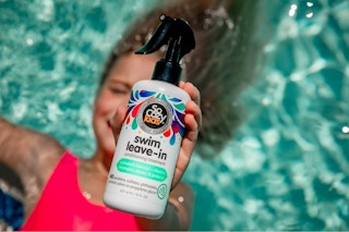 a girl holding the SoCozy Kids' Swim Leave In Conditioner Spray in a swimming pool