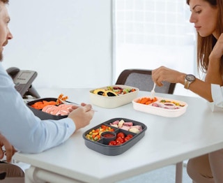 two people eating food in bento boxes at a table