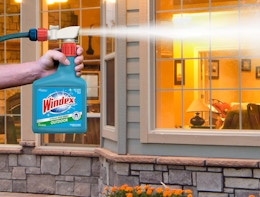 a person spray Windex on the outside of a window 