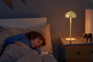 a girl sleeping next to a table lamp