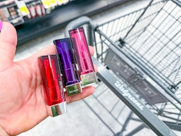 hand holding maybelline color sensational lipsticks over walgreens cart