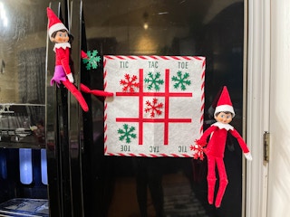 two elf on the shelf dolls playing tic tac toe on fridge