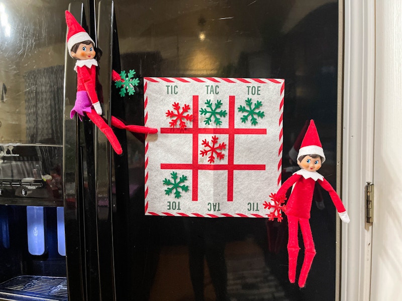 two elf on the shelf dolls playing tic tac toe on fridge