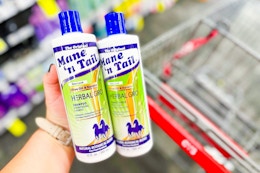 person holding 2 bottles of mane n tail shampoo over a cart