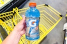 hand holding a bottle of gatorade above a dollar general shopping cart