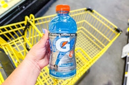 hand holding a bottle of gatorade above a dollar general shopping cart