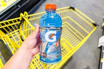 hand holding a bottle of gatorade above a dollar general shopping cart