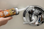 person apply silicone sealant to shower handle