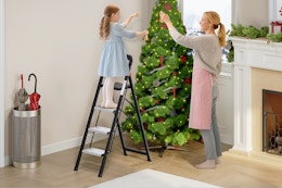 mother and daughter using ladder to decorate Christmas tree