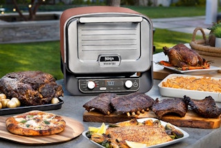 a ninja outdoor oven and smoker with food around it 