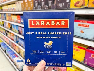 A Larabar box held out by hand in front of store shelves with other food products on them.