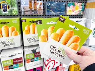 a person holding two olive garden gift cards in front of a lot of gift cards in store display