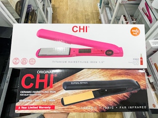 A pink Chi Titanium Hairstyling Iron box and a Chi Original Ceramic Hairstyling Iron held out in front of store floor and aisle.