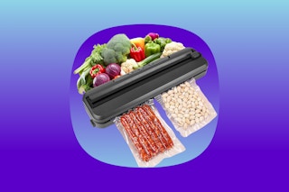 A black vacuum sealer seals some meat sticks and some nuts. Raw veggies are arranged on the other side of it.