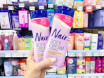 hand holding two bottles of nair body cream in walmart aisle