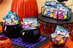 A Halloween snack table in orange, black and purple with pumpkins, spiders, and cauldrons full of Nerds, Trolli and Now and Later candy.
