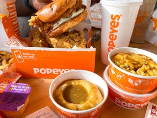 A close up of a table of Popeyes food including a chicken sandwich, sides, and a Popeyes drink cup.