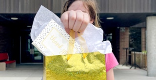 tween child holding a gold gift bag with thank you card outside school
