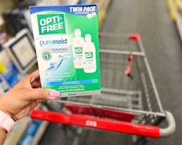 hand holding one box of opti-free pure moist solution in front of shopping cart