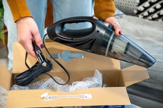 A person taking a ThisWorx handheld vacuum cleaner out of a box.