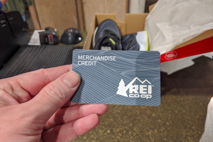 Hand holding REI merchandise card at customer service counter