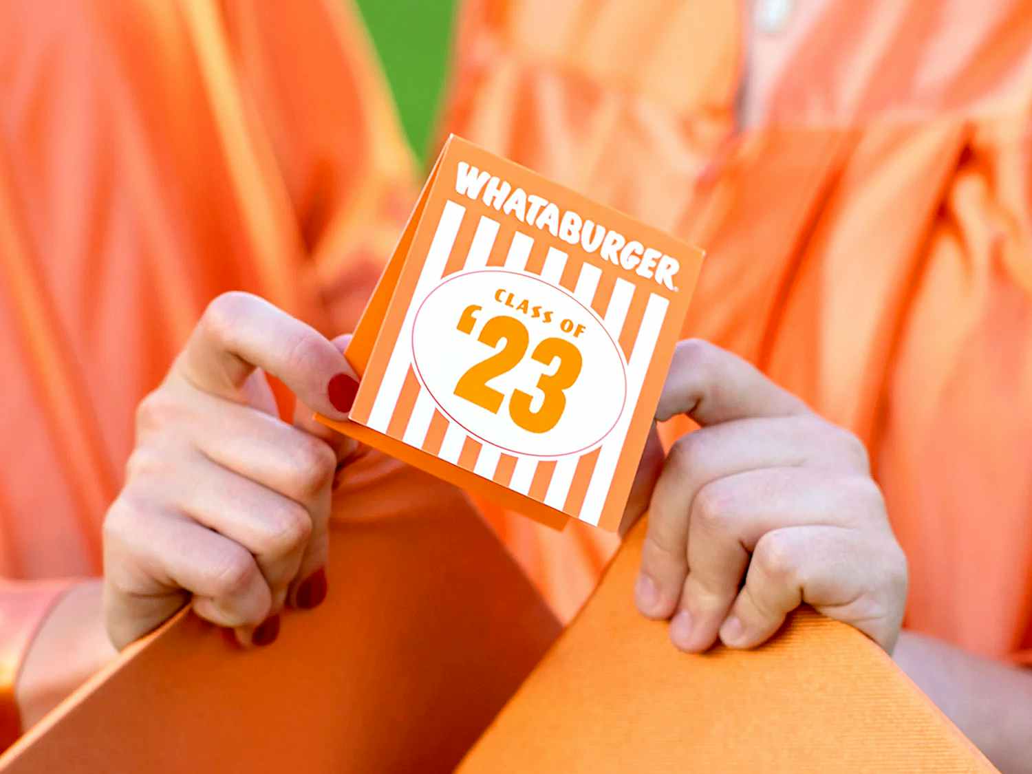 two graduates holding their caps and a class of 2023 whataburger table tent