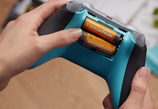 a hand putting amazonbasics batteries into a gaming controller