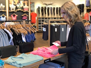 Woman looking at a stack of tank tops as if she's deciding on a color