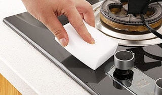 person using melamine magic sponge on a stovetop