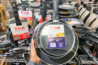 a t-fal frying pan set held up in front of a display of other pan sets in macys