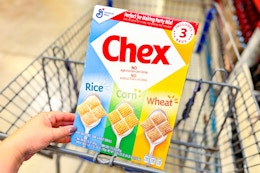 hand holding a box of chex cereal over shopping cart