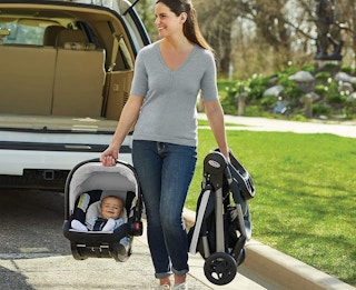 A woman carrying a Fast Action Graco stroller and car seat.