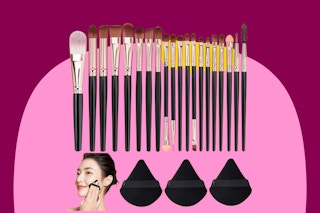 Twenty makeup brushes with reddish purple handles of varying size are lined up below three triangular purple powder puffs.
