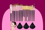 Twenty makeup brushes with reddish purple handles of varying size are lined up below three triangular purple powder puffs.