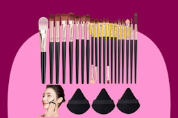 Twenty makeup brushes with reddish purple handles of varying size are lined up below three triangular purple powder puffs.