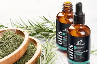 Two bottles of rosemary aromatherapy oil sit next to rosemary sprigs and ground rosemary