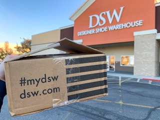 A DSW.com shipping box held in front of a DSW store.