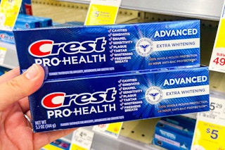 hand holding two boxes of crest toothpaste next to shelf with sales tags