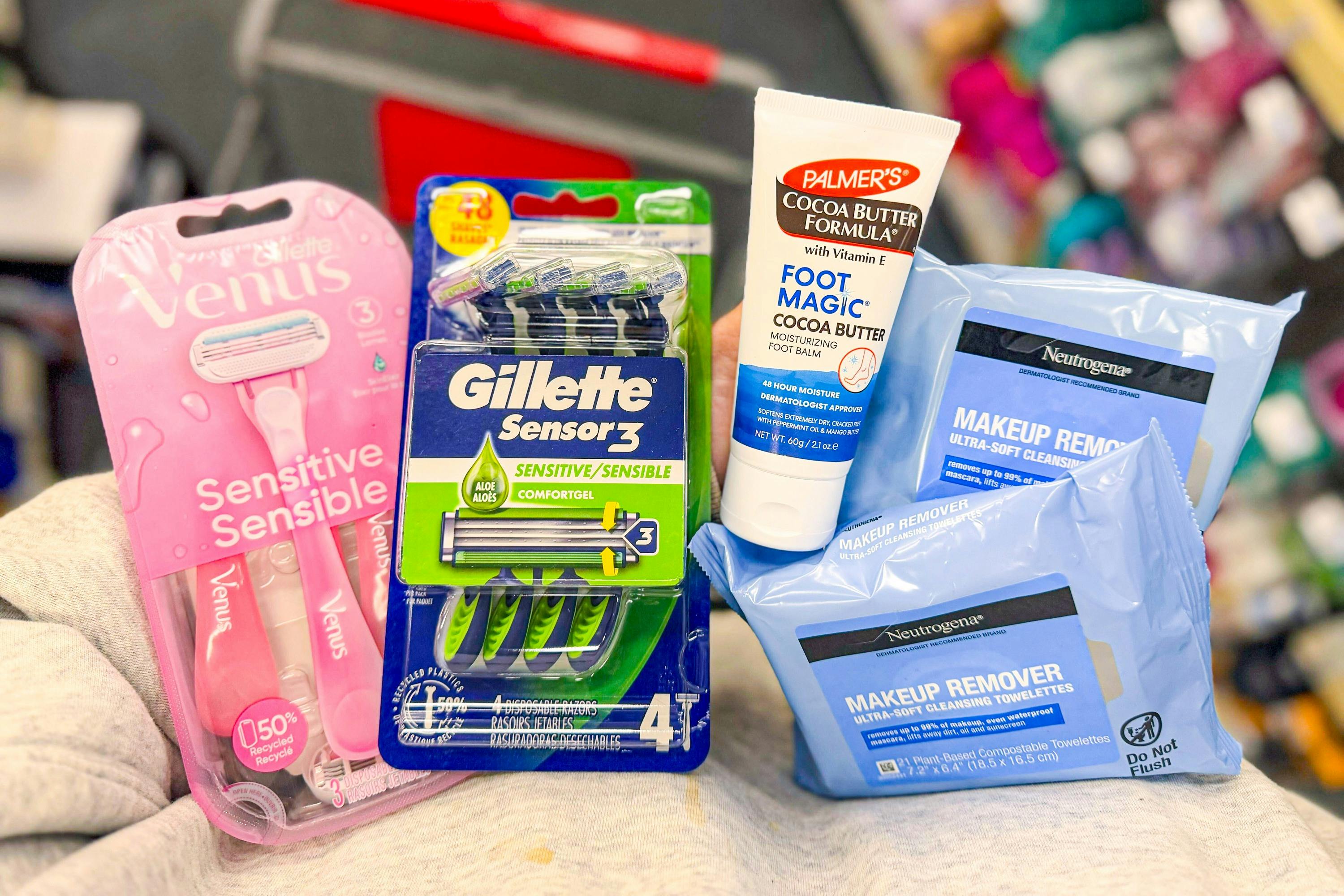 person holding neutrogena makeup wipes, palmers foot cream, and gillette and venus razor packs