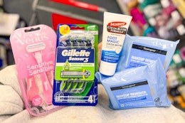 person holding neutrogena makeup wipes, palmers foot cream, and gillette and venus razor packs